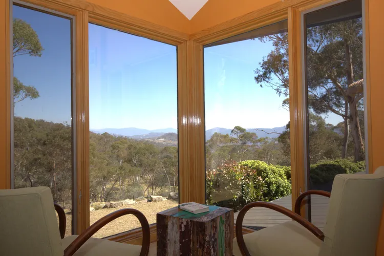 Corner seating area with light chairs and a rustic stump table inside orange-walled room; bay windows frame trees and distant hills outside.