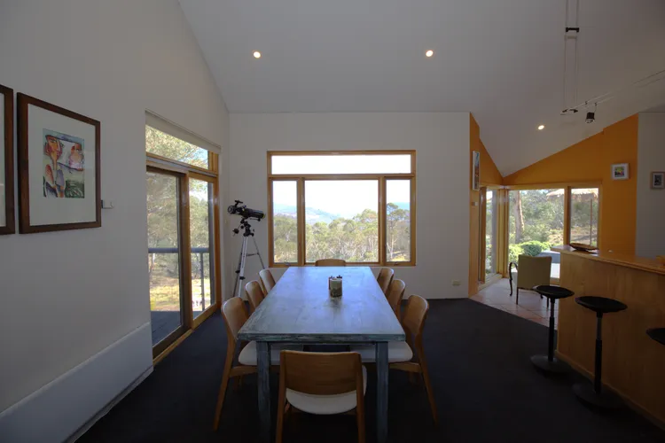 Bright dining room with a long table and chairs, a telescope by the window, and a bar area to the right.
